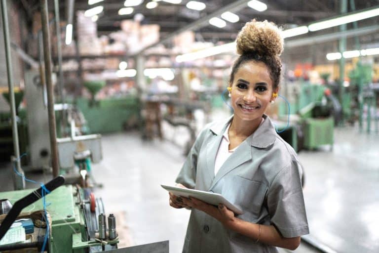 Woman standing inside a industrial factory. She is holding a tablet.